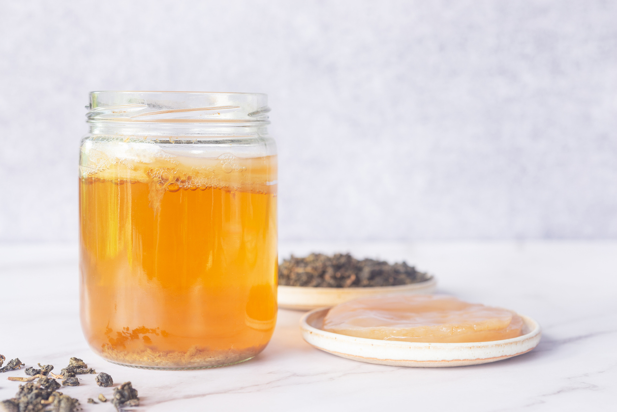 kombucha starter in a glass jar bottle with healthy Kombucha SCOBY symbiotic culture of bacteria and yeast in white ceramic plate and oolong loose leave tea on white marble background, how to brew kombucha at home.